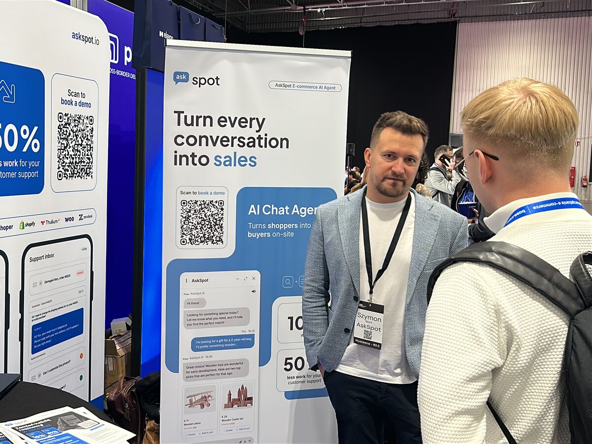 Szymon Spyra z AskSpot rozmawia z odwiedzającym, widocznym od tyłu, na stoisku AskSpot na E-commerce Warsaw Expo 2026